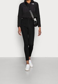 Sudadera de felpa negra corta con cuello alto, combinada con leggings negros de tiro alto y zapatillas blancas. Pequeño bolso negro cruzado.