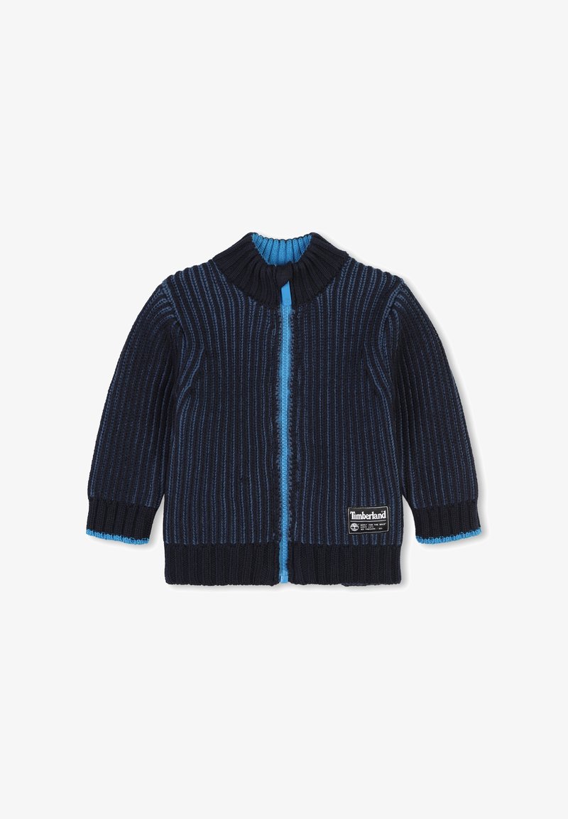 Cardigan lavorato a maglia blu navy con righe verticali, colletto blu e dettagli con zip, e logo Timberland in basso a destra. Texture morbida.