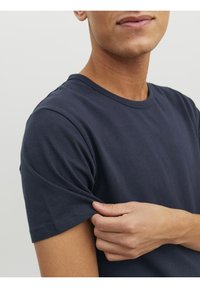 Marinblå T-shirt med kort ärm, tillverkad av bomull, med rund halsringning och en mjuk textur, visad med en hand som rör vid ärmen.