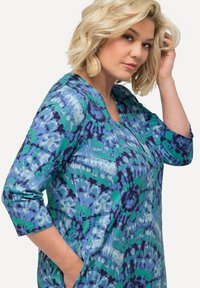 Top a maniche lunghe colorato con un motivo tie-dye blu-verde, scollatura rotonda e tasche laterali, realizzato in un materiale morbido.