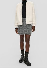 Krämfärgad, fluffig bomberjacka med elastiska ärmar, ihop med en svart polotröja och en strukturerad minikjol i svart och vitt. Svarta klumpiga stövlar.