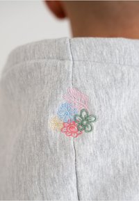 Tessuto grigio con una texture morbida, caratterizzato da un ricamo floreale colorato in rosa, blu, verde e giallo sulla cucitura della spalla.