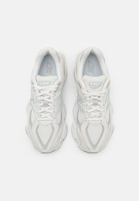 Valkoiset urheilukengät, joissa on verkkokudosta ja synteettistä materiaalia, kevyillä sinisillä yksityiskohdilla, pyöreällä varvassuojalla ja vaimennetulla pohjalla.