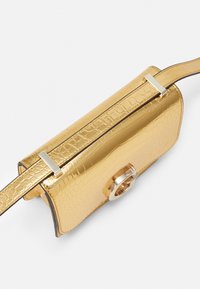 Guldmetal taske med krokodillemønster, rektangulær form, sølv hardware accenter og en flad justerbar rem.