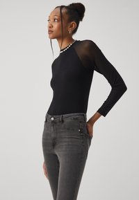 Μαύρο κορμάκι με μακριά μανίκια και διαφανή πλέγμα, σε συνδυασμό με σκούρες γκρι εφαρμοστές τζιν σε παντελόνι με τσέπες και κλείσιμο με κουμπί.