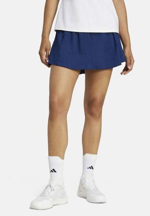 Marineblauwe sportrok met een uitlopende pasvorm, gemaakt van lichtgewicht materiaal. Gecombineerd met witte sneakers en enkelsokken met zwarte strepen.