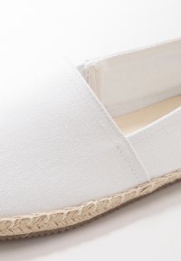 Espadrille en toile blanche avec une semelle en corde de jute au fini texturé. Le design présente un style simple à enfiler et des coutures minimales.