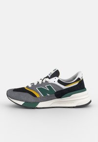 Tenisky New Balance s vrškem z šedé semišové a síťoviny, zelenými akcenty, žlutým pruhem a bílou mezipodešví s texturovanou černou gumovou podešví.