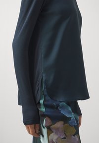 Pitkähihaisessa tummansinisessä kankaassa on sileä pinta, ja siinä on sivuaukot. Yhdistetty kukkakuosisin värikkäisiin housuihin.