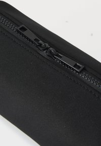 Black fabric pouch featuring a smooth texture and a black zipper with two pulls, set against a white background.