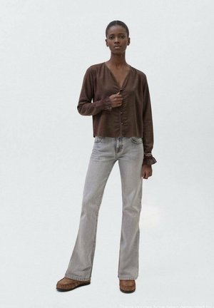 Blouse marron, texturée, à manches longues avec un boutonnage sur le devant, associée à un jean flared taille haute gris clair et des chaussures de style moccasin marron.