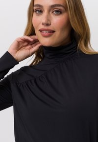 Black high-neck top with gathered texture and smooth fabric. Features a fitted silhouette and long sleeves, showcasing a sleek design.