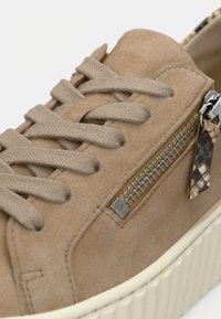 Baskets en daim beige à surface texturée, avec lacets plats, détail zippé argenté, et une semelle en caoutchouc blanche contrastante.