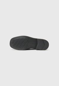Black shoe sole featuring textured rubber with angular grooves and a rectangular shape. The heel is slightly elevated.