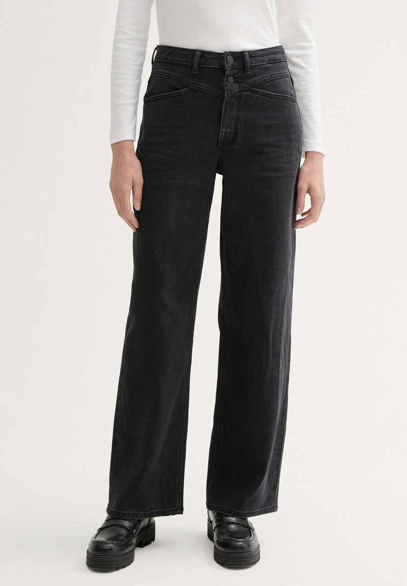 Jeans de mezclilla negros de talle alto con piernas anchas, que presentan costuras distintivas y un cierre de dos botones. Textura suave, acentos mínimos.