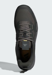 Grå trail-løbesko med en åndbar mesh-overdel, tekstureret overflade, snørebånd og en fremtrædende hælflap med logodetalje.