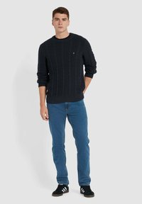 Marineblauw kabelgebreid trui met een ronde halslijn, gedragen met blauwe jeans en zwarte sneakers. Bevat textuurpatronen en geribbelde manchetten.
