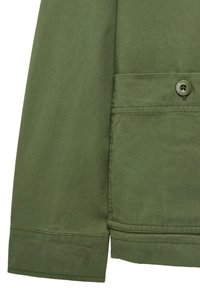Olivengrøn jakke med detaljer, der viser en flad lomme med knaplukning og manchetter. Jakken er lavet af et glat stof med synlige syninger.