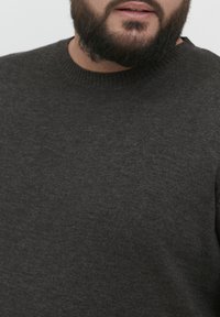 Pull gris foncé avec un col rond. Le tissu a une texture douce, présentant un motif en tricot subtil.