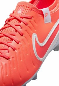 Felle roze voetbalschoen met een gestructureerde synthetische bovenkant, witte swoosh-logo en grijze noppen. Beschikt over een gevoerde kraag en nauwkeurig geweven veters.