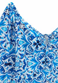 Tissu bleu et blanc à motifs floraux et géométriques, avec un col élastique froncé et un petit détail de nœud devant.