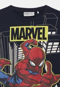Camiseta de algodón azul marino con un gran gráfico de Spider-Man en rojo y azul, con texto en amarillo y negro que dice "MARVEL". Textura suave.