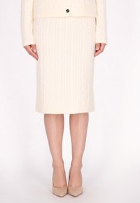 Strickrock in Creme mit Zopfmuster, taillierte Silhouette, knielang, mit geripptem Saum, kombiniert mit beigen spitzen High Heels.