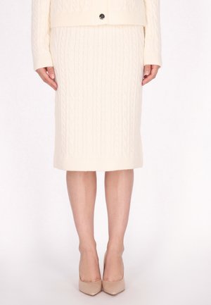 Strickrock in Creme mit Zopfmuster, taillierte Silhouette, knielang, mit geripptem Saum, kombiniert mit beigen spitzen High Heels.
