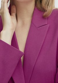 Fuchsiasjacket med skarpa slag och en något texturerad yta. Har en djup V-ringning och strukturerade axlar för en skräddarsydd look.