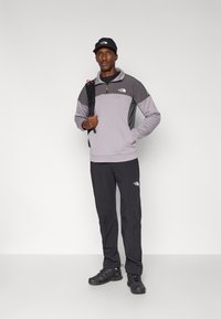 Gray and black fleece pullover with a half-zip, black pants, and shoes. Accessories include a black cap and a backpack, featuring logos.