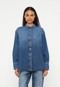 Πουκάμισο από τζιν σε σκούρο μπλε χρώμα, με ψηλό γιακά, κλείσιμο με κουμπιά και μακριά μανίκια. Λεπτομέρεια με λογότυπο στο στήθος, άνετη εφαρμογή.