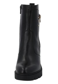 Bottes chevilles noires en cuir avec une texture lisse, fermeture éclair sur le côté et clous décoratifs en ton doré. Dotées d'une épaisse semelle noire pour la stabilité.