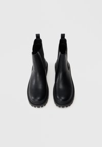 Botas de tobillo de cuero negro con un acabado suave, paneles laterales elásticos y suelas de goma texturizadas. Diseño minimalista, forma de punta redondeada.