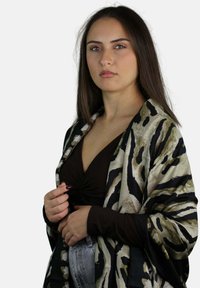 Sciarpa nera e beige con motivo astratto, indossata sopra una maglia marrone e jeans di denim, con una texture leggera.