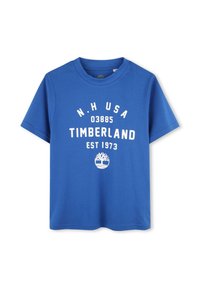 Camiseta de algodón azul con mangas cortas, cuello redondo, que presenta un texto impreso en blanco "N.H USA 03885 TIMBERLAND EST 1973" y un logotipo.