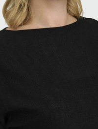 Melnas teksturētas auduma blūze ar brīvu, plašu kakla izgriezumu un relaksētu piegriezumu, kuram ir neliels ribojošs raksts ap apkakli.