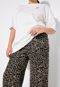 T-shirt bianca oversize con grafica rossa "Ti ❤️ amo", abbinata a pantaloni wide-leg in stampa leopardata marrone e nera, con texture liscia.