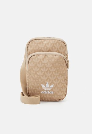 Sac bandoulière beige Adidas avec sangle ajustable, poche avant zippée et motif répétitif du logo trèfle.