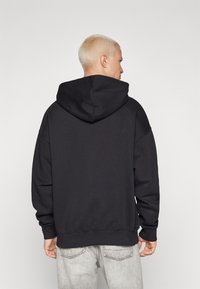 Zwarte hoodie met een grote, zachte capuchon, een relaxte pasvorm, ribgebreide manchetten en zoom. Draagt samen met lichtgekleurde, versleten jeans.
