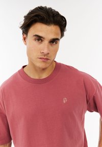 Korte mouwen, ronde hals t-shirt in stofroze katoen, met een klein logo op de borst in een contrasterende textuur. Gladde stofafwerking.