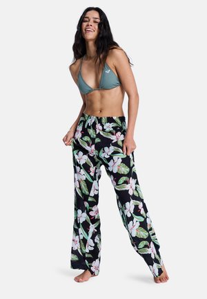 Letvægts, sorte bukser i stof med blomsterprint, løstsiddende pasform og elastisk talje, med store hvide og grønne blomster.