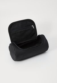 Black zippered cosmetic bag with a rounded shape, made of textured fabric. Features an inner mesh pocket and a spacious main compartment.