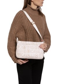 Borsa bianca con una texture liscia, caratterizzata da un motivo logo stampato in beige su tutta la superficie. Presenta una tracolla staccabile e una chiusura con zip.