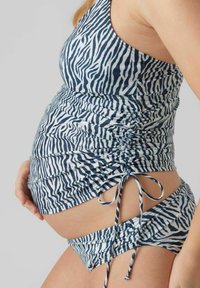 Gravidbaddräkt i marinblå och vit zebramönster, med rynkad design, sidoknytningar och ett elastiskt tyg som rymmer en växande mage.