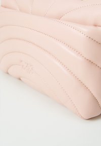 Rozā ādas rokassoma ar viļņotu quilted dizainu un redzamām šuvēm. Noapaļota forma ar maigu izspieduma logotipa detalizāciju. Gluda tekstūra.