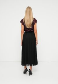 Black pleated skirt with a sheer layer, paired with a maroon satin top featuring lace details on the short sleeves. Black high heels.