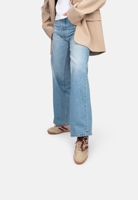 Jeans a gamba larga di colore azzurro chiaro abbinati a un blazer over size beige e sneakers beige con accenti bordeaux e lacci testurizzati.