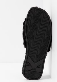 Semelle d'une pantoufle noire duveteuse avec motif de grip incurvé et logo KARL LAGERFELD sur fond blanc.