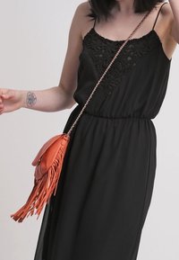 Černé šaty s korzetem lemovaným krajkou a ramínky na tenké šňůrky. Oranžová kožená kabelka přes rameno s dlouhými třásněmi.