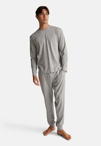 Top ligero de manga larga gris combinado con pantalones de pijama a juego, ambos con corte relajado y puños de canalé, fabricados en tejido suave.